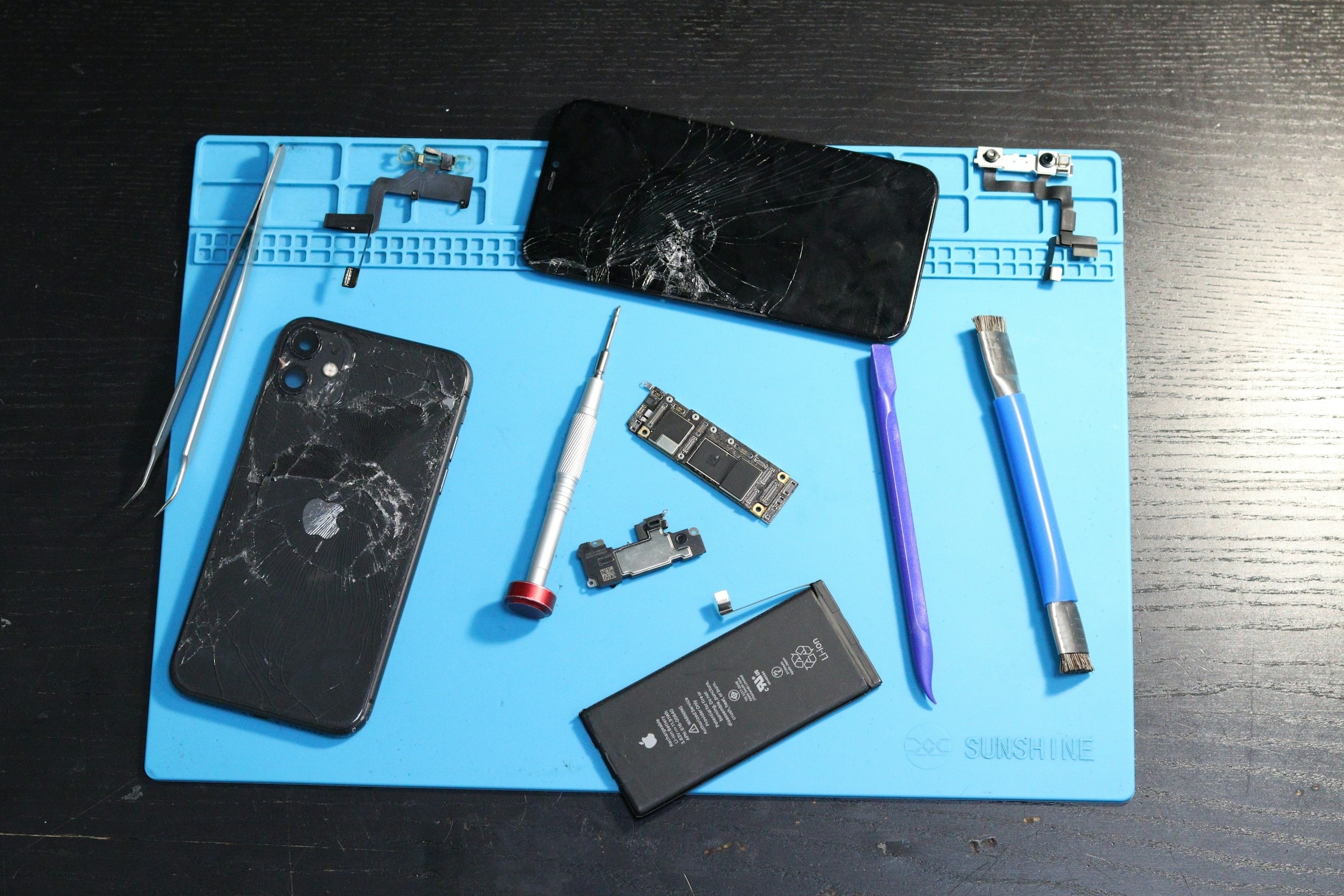 A cracked iPhone taken apart on a repair mat with tools